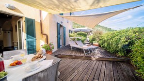 Une terrasse en bois avec des chaises longues, une table garnie de nourriture et de boissons, et un espace ombragé sous une tonnelle.