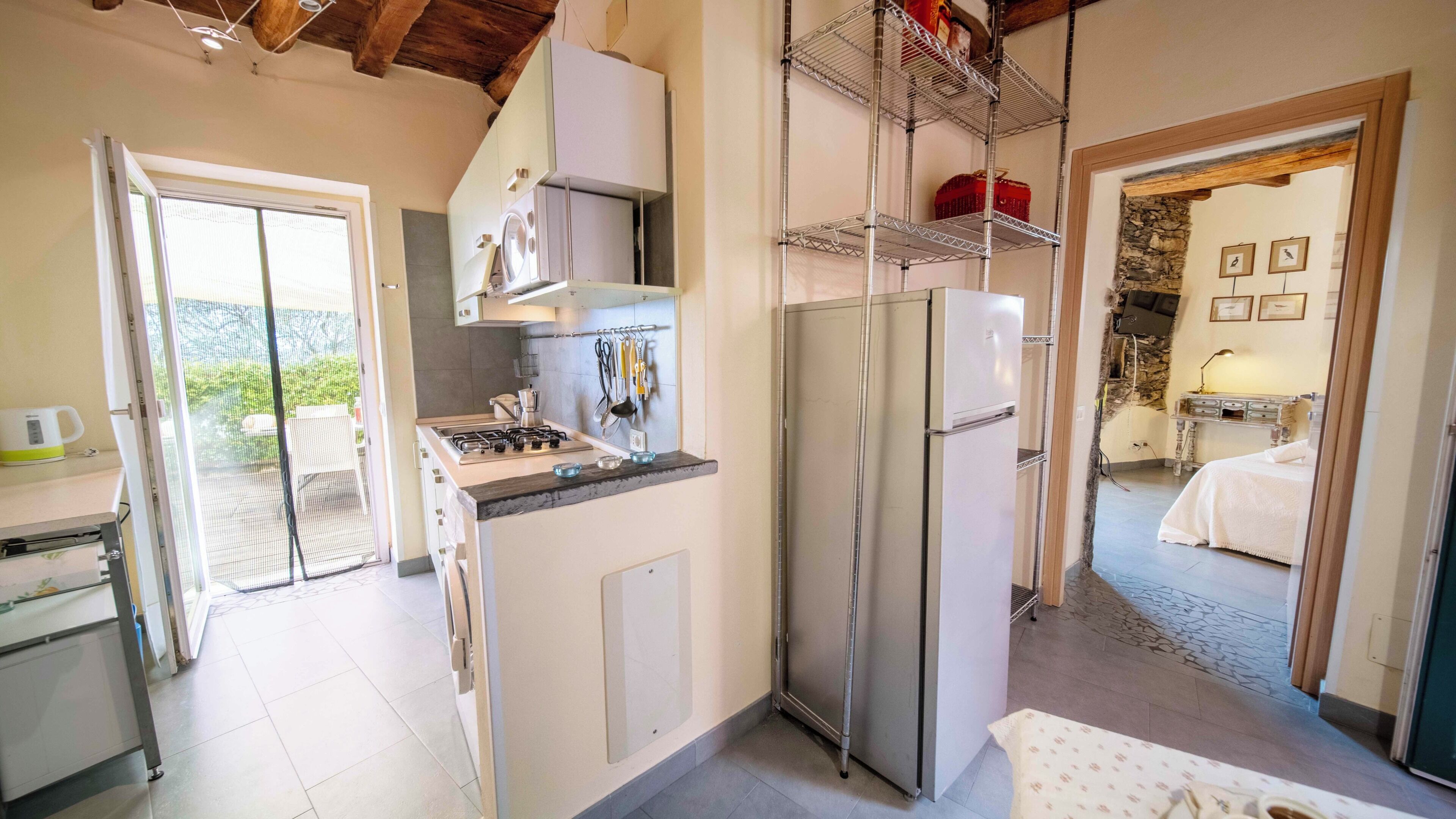 A compact kitchen with a gas stove, a refrigerator, and a sink. There is a balcony door leading to an outdoor area.