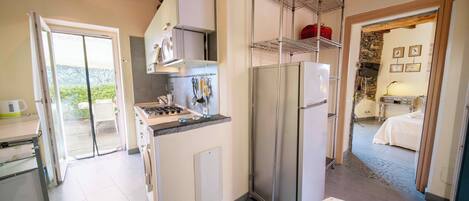 A compact kitchen with a gas stove, a refrigerator, and a sink. There is a balcony door leading to an outdoor area.