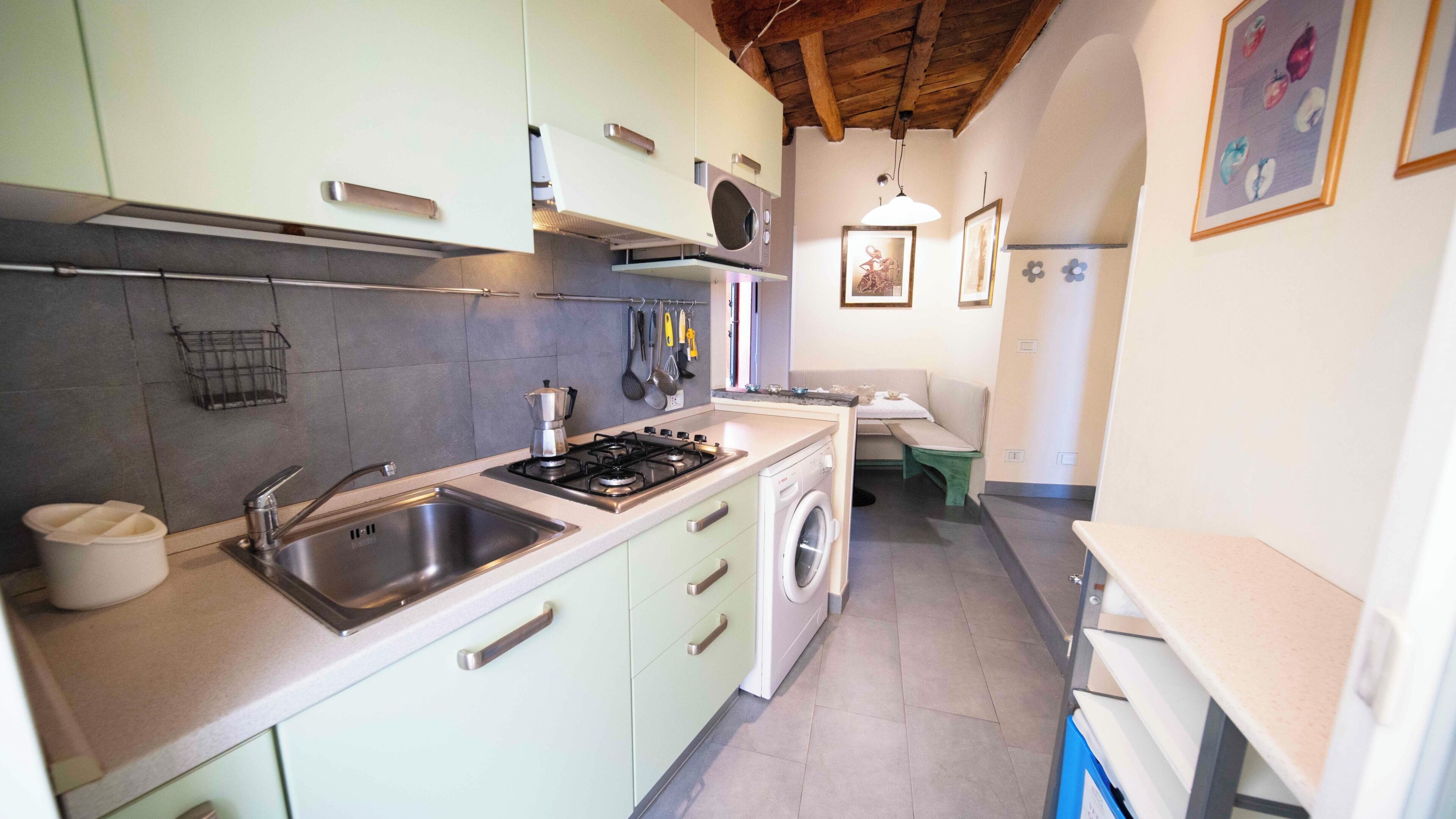 Une cuisine compacte comprenant un évier, une cuisinière et un lave-linge, un petit coin repas et un banc.