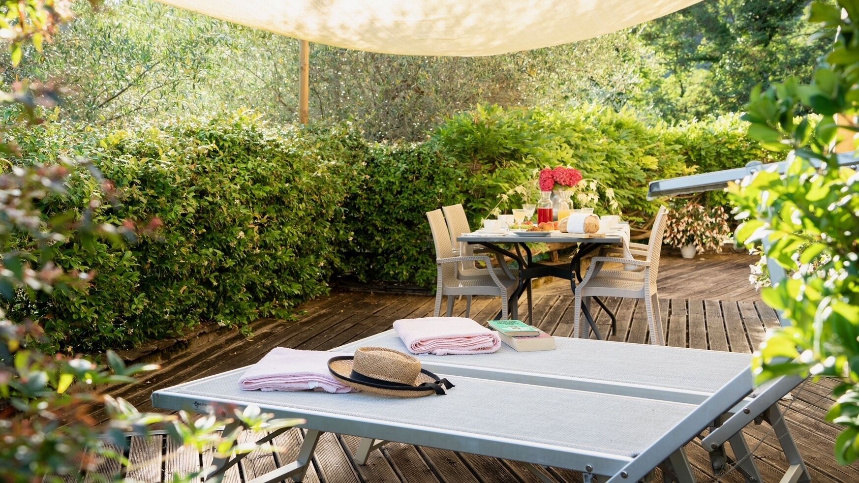An outdoor patio with a table set for two, surrounded by greenery.