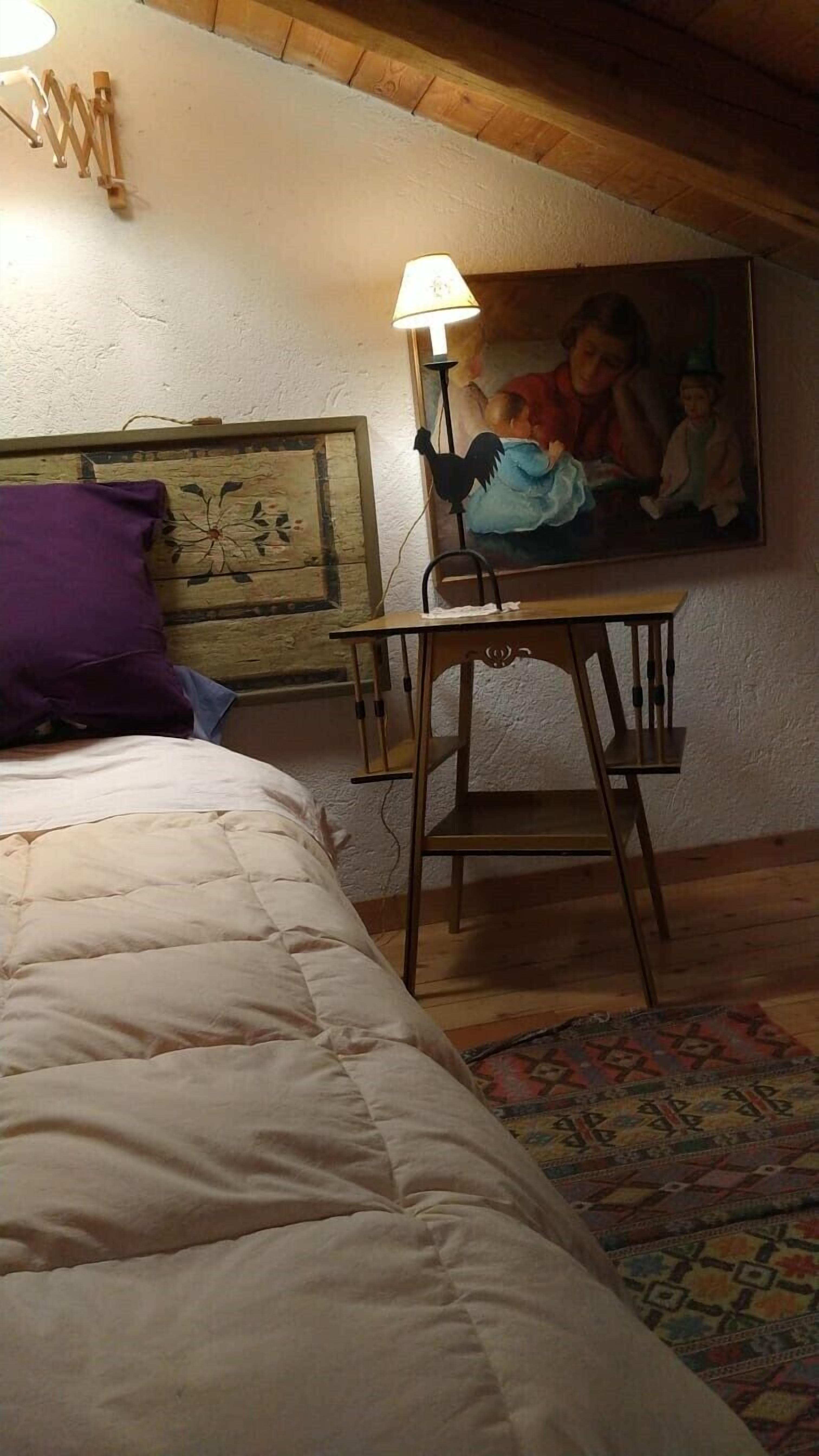 Een slaapkamer met een bed, een houten bureau, een lamp, een schilderij en een vloerkleed met dessin.