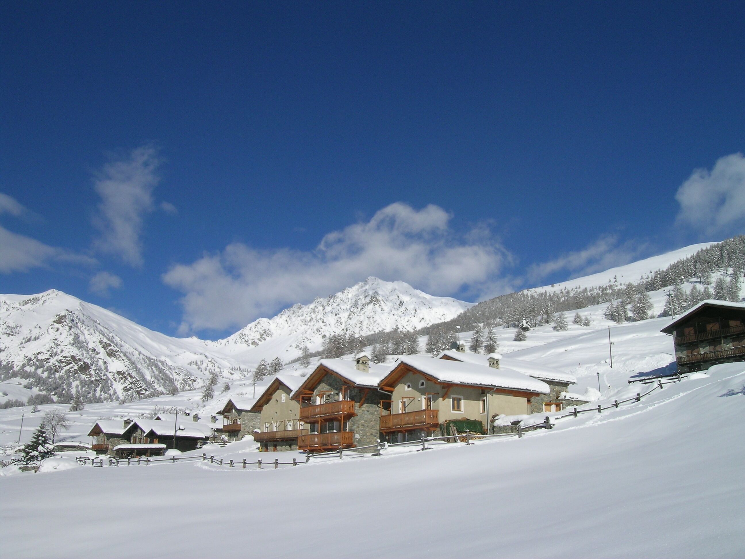 A snow-covered mountain resort with chalet-style buildings, wooden balconies, and a clear blue sky.