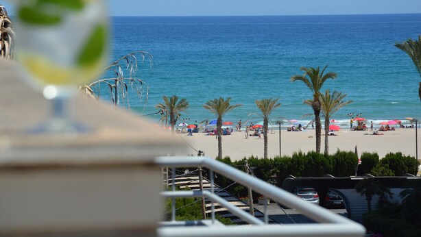 A beach view with palm trees, umbrellas, and people. -  PENTHOUSE WITH LARGE TERRACE, SEA VIEWS, ONE STEP FROM THE BEACH AND WIFI (Campello)