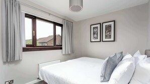 A bedroom with a large bed, a window with curtains, a radiator, and two framed pictures on the wall.