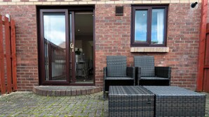 A brick building with a sliding glass door leading to an interior space, a window with a dark frame, and outdoor wicker furniture.