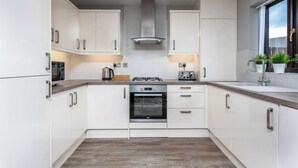 A modern kitchen with white cabinets, a stainless steel range hood, a built-in oven, and a window with plants.