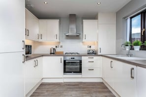 Una cocina moderna con armarios blancos, una campana extractora de acero inoxidable, un horno empotrado y una ventana con plantas.