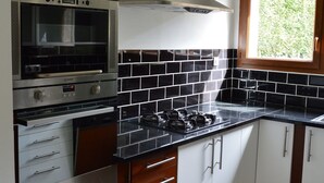 Une cuisine équipée d’un four, d’un micro-ondes et d’une cuisinière encastrés, de meubles blancs et d’un dosseret de carrelage noir.