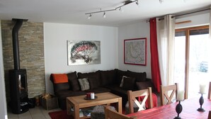 Un salon avec un canapé marron, une table basse en bois et un tapis rouge. On y trouve une cheminée, une carte accrochée au mur et une fenêtre avec des rideaux.