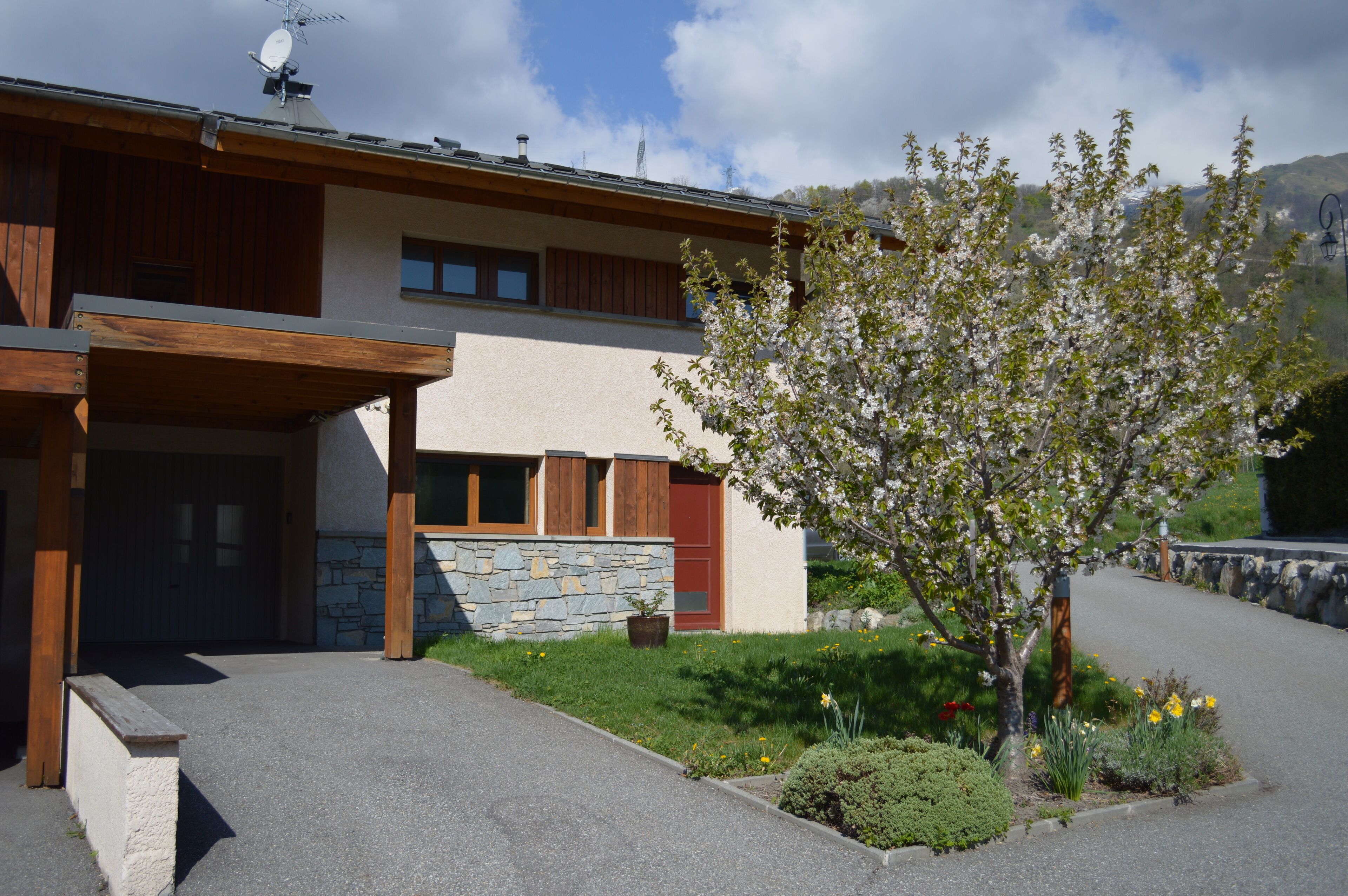 Une maison moderne avec une façade en pierre, des poutres en bois et un porche abrité.