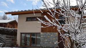 Une maison moderne à deux étages, dotée d’une façade en pierre, de grandes portes-fenêtres coulissantes et d’une terrasse en bois.