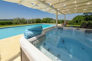 A hot tub with a towel, a pool, and a pergola with a view of the landscape.