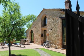 A stone building with arched doorways, a patio with outdoor seating, and a bicycle parked outside.