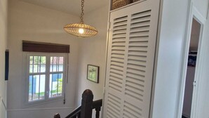 A staircase with wooden steps and a dark wooden railing, leading to a white closet with louvered doors and baskets on top.