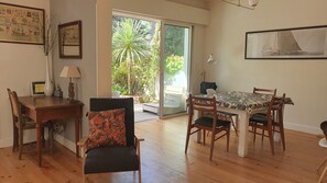Uma sala de jantar com uma mesa e cadeiras, uma cadeira com almofada estampada, um abajur e um quadro na parede.
