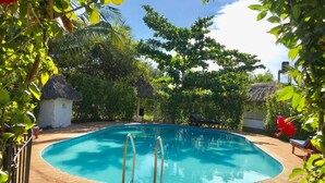 A swimming pool surrounded by lush greenery and a thatched-roof structure.