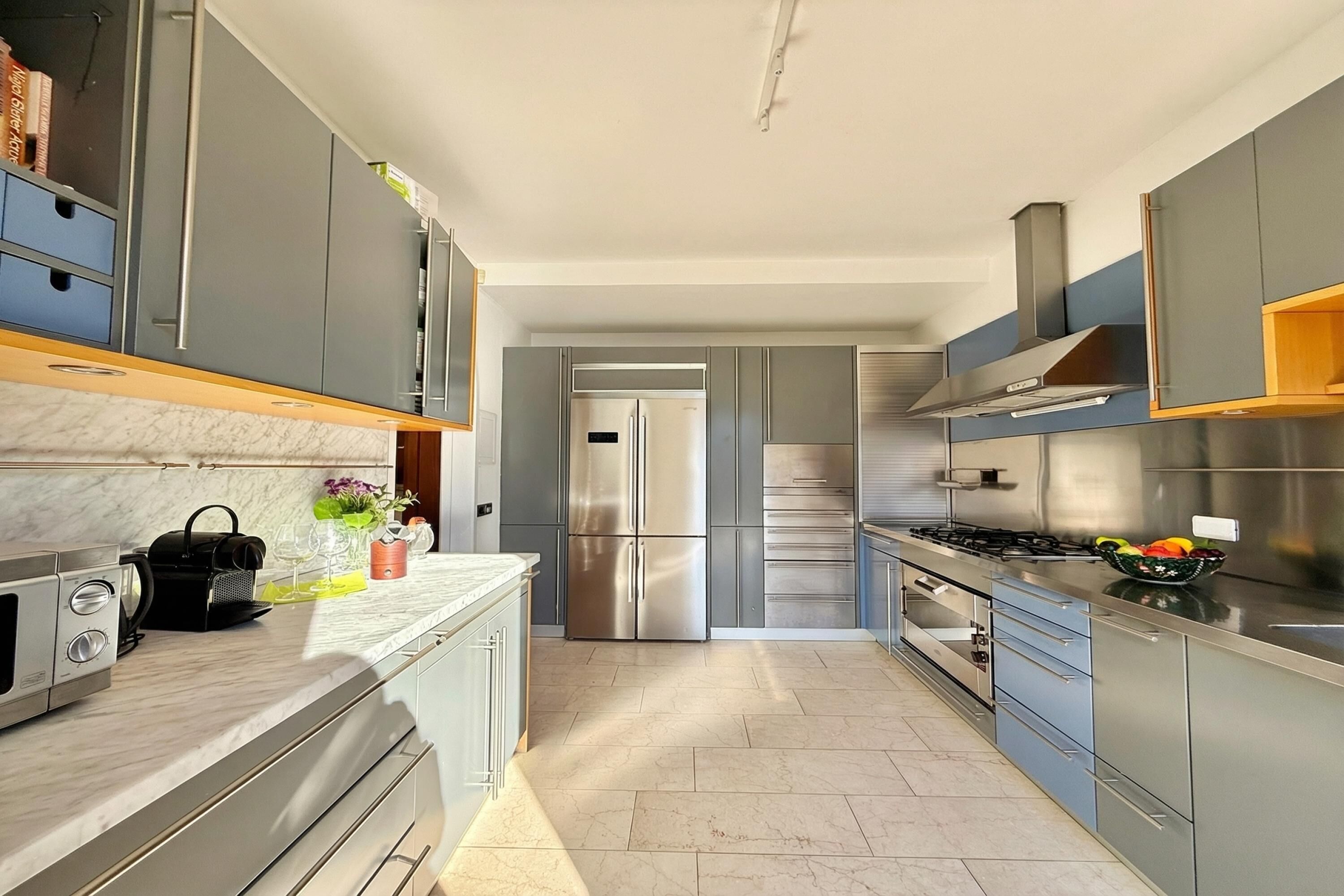 Une cuisine moderne avec des meubles gris, des appareils en acier inoxydable et un plan de travail en marbre.