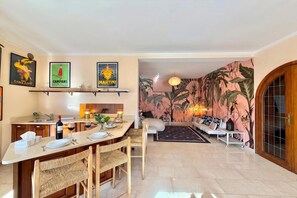 Un espacio habitable moderno con área de cocina, una mesa de comedor para dos personas y una sala de estar con sofá y pared decorada.