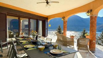 Une terrasse avec une table dressée pour le repas, des chaises en osier, un ventilateur de plafond et une vue sur les montagnes.
