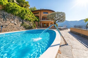 Una piscina con fuente, un muro de piedra y un edificio con balcones al fondo.