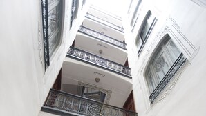 Un interior de varios niveles con una imponente escalera, barandales ornamentados y una serie de ventanas.