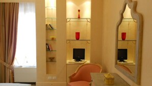 Ein Hotelzimmer mit einem Bett, einem Sessel, einem Schreibtisch, einem Spiegel und Regalen mit Büchern und Dekoration.