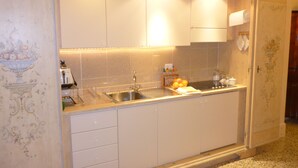 Eine kleine Küche mit weißen Schränken, einer Edelstahl-Spüle und einer Arbeitsplatte mit einem Toaster und einer Fruchtschale.