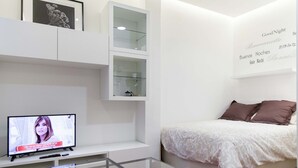 Une chambre à coucher moderne avec un lit, une table basse en verre, un téléviseur et des étagères intégrées.