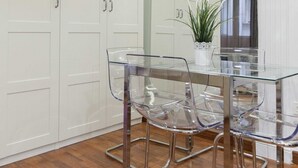 Un coin repas avec une table et des chaises en verre, des meubles blancs et une plante en pot.