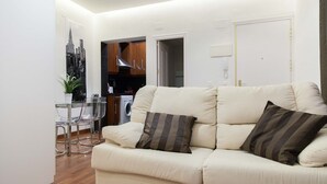 Un salon avec un canapé beige, deux coussins à rayures, une table basse en verre et une plante en pot.