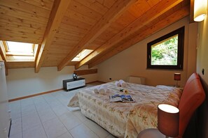 Una camera da letto con soffitto spiovente, un letto con copripiumino floreale, una lampada da comodino e una finestra vista verde.