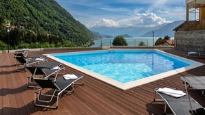 A swimming pool with lounge chairs, surrounded by a wooden deck and overlooking a mountainous landscape. - Residence Eden Gardenia 11, Argegno, Italy (Argegno)