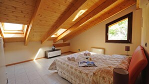 A bedroom with a wooden ceiling, a bed with a floral bedspread, a window, and a nightstand. - Residence Eden Gardenia 11, Argegno, Italy (Argegno)