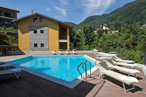 A swimming pool with lounge chairs, a building with a stone facade, and a mountainous backdrop.