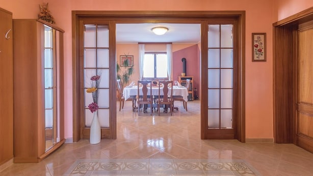 Un couloir mène à une salle à manger dont le sol est recouvert de carreaux et où se trouve un vase rempli de fleurs.