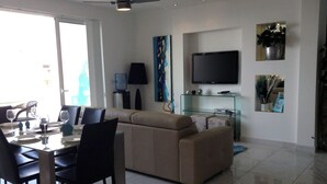 A modern living room with a dining area, a sofa, a TV, and a glass cabinet. - LUXURY SEAFRONT APARTMENT WITH POOL (Saint Paul's Bay)