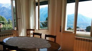 A dining area with a round table, chairs, and a view of mountains through large windows. - SPLENDID VIEW OF LAKE COMO bellagio / civenna (Civenna)