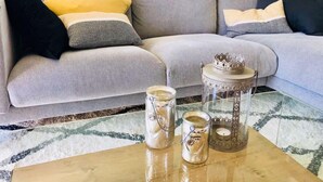 A living room with a grey sofa, yellow and black cushions, a coffee table with two glass jars and a decorative lantern.