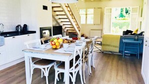 A dining area with a wooden table and white chairs, a fruit bowl, and a staircase leading to an upper level.