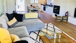A modern living room with a grey sofa, a glass coffee table, and a dining area with a white table and chairs.