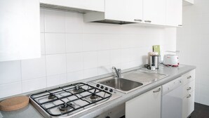 Una cucina con mobili bianchi, un fornello a gas, un lavello e una macchina per il caffè.