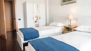Una camera d'albergo con due letti, un armadio, un comodino con una lampada e un quadro appeso al muro.