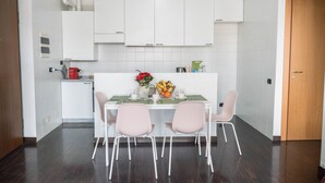 Una cucina moderna con mobili bianchi, un tavolo da pranzo con due sedie rosa e una ciotola di frutta sul piano di lavoro.