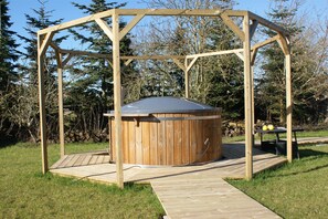 Een houten jacuzzi met een pergola, omringd door gras en bomen.