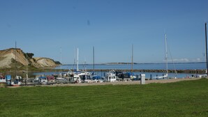 A marina with boats docked, a grassy foreground, and a rocky shoreline in the background. - Wonderfull holiday house                                           (Nykøbing Mors)