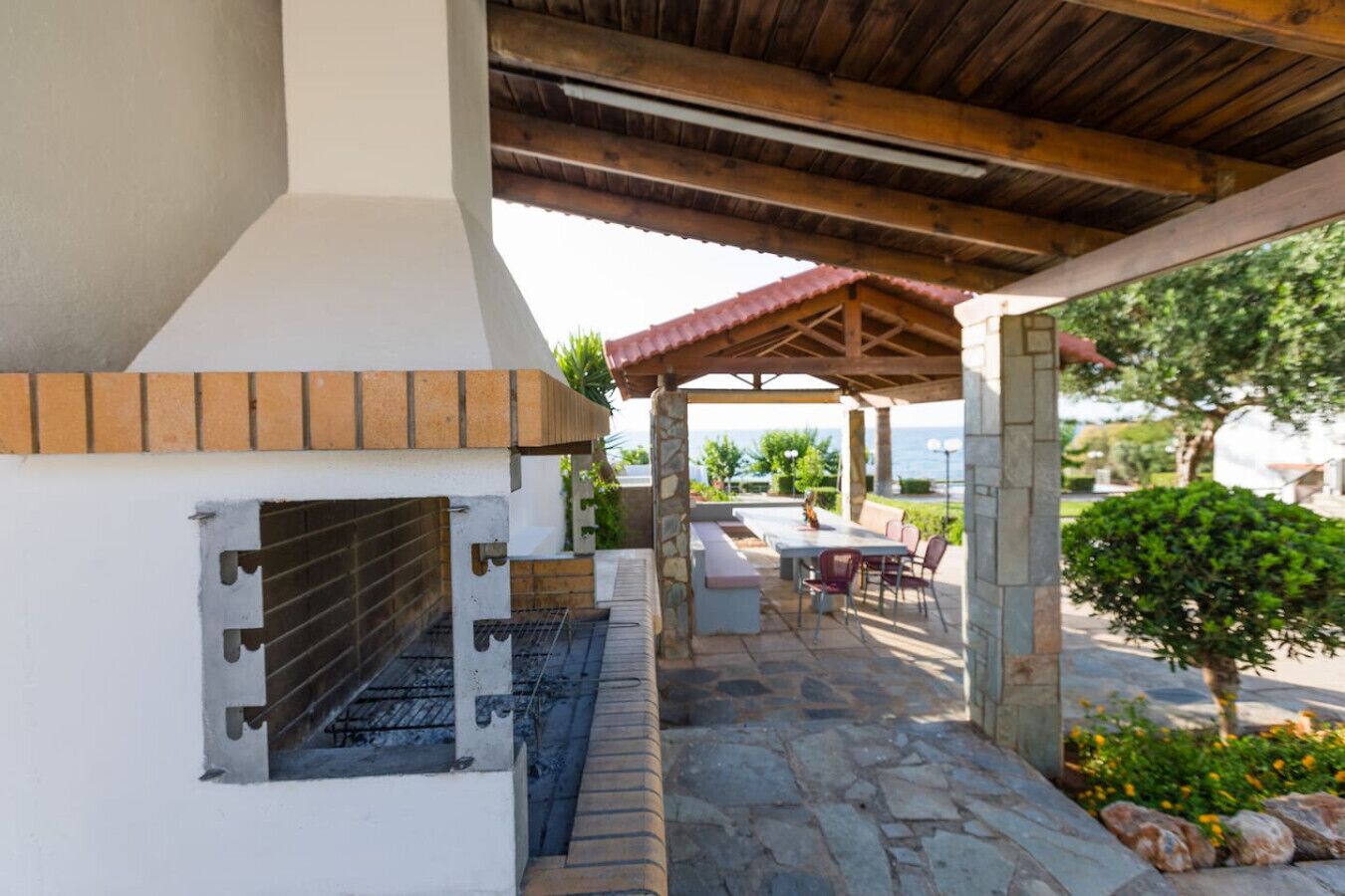 Un espacio al aire libre techado con una parrilla, piso de piedra y un conjunto de asientos.