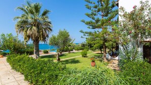 A garden with a palm tree, a pool, and a white building. - Family Beachfront Villa w/Private Pool & Play Area (Rethymno)