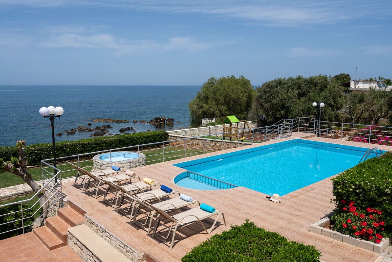 A swimming pool with a view of the sea, surrounded by lounge chairs and a children's play area.