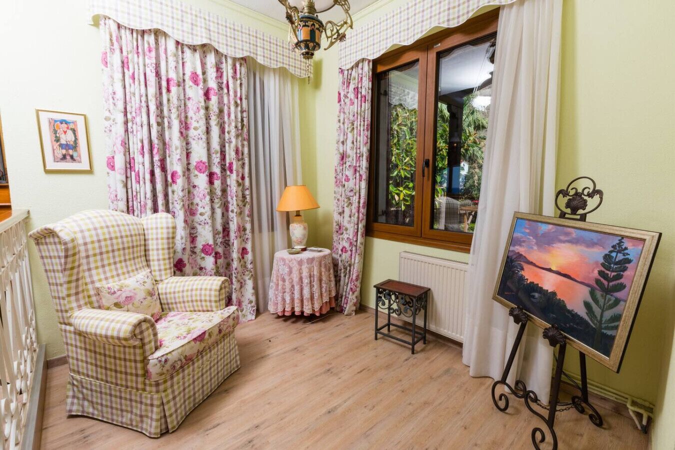 Een kamer met een kamer met een geruit fauteuil, een tafeltje met een lamp, een schilderij op een standaard en een raam met gordijnen.